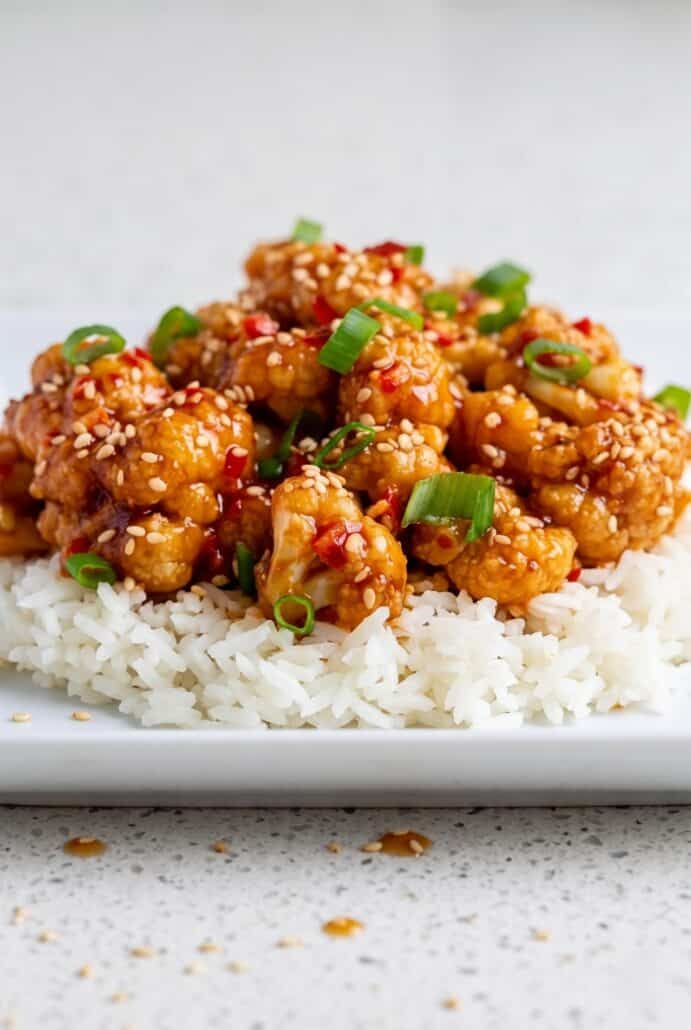 Sticky sesame cauliflower piled on fluffy jasmine rice with sesame seeds and green onions for an easy vegetarian takeout-style meal.