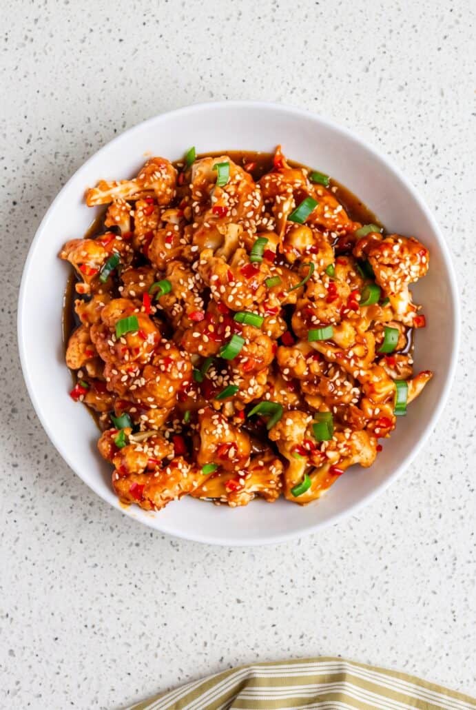 Sticky sesame cauliflower garnished with sesame seeds, green onions, and red chilies for an easy takeout-style vegetarian meal.