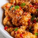 Sticky sesame cauliflower topped with sesame seeds, red chilies, and green onions.