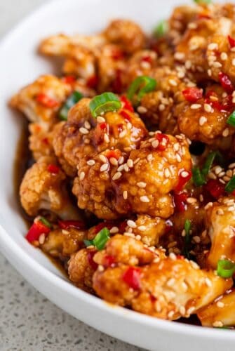 Sticky Sesame Cauliflower Recipe - Better Than Takeout! Sticky sesame cauliflower topped with sesame seeds, red chilies, and green onions.
