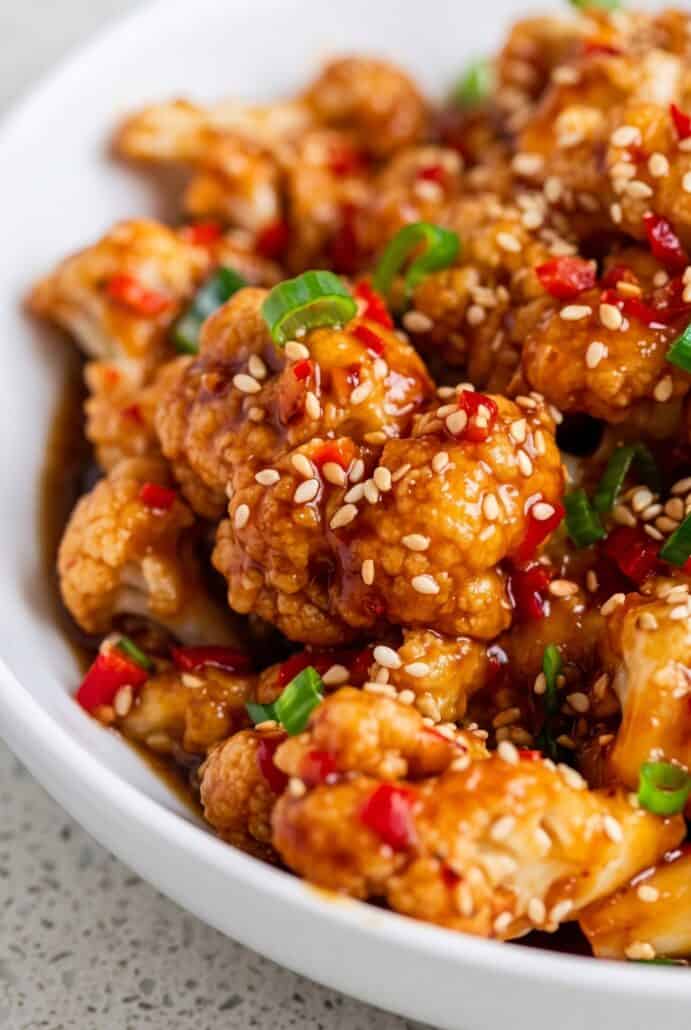 Sticky sesame cauliflower topped with sesame seeds, red chilies, and green onions.