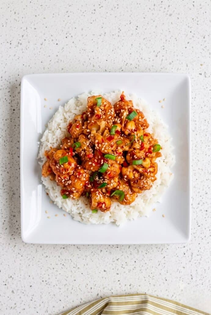 Sticky sesame cauliflower served over jasmine rice with sesame seeds, green onions, and red chilies.