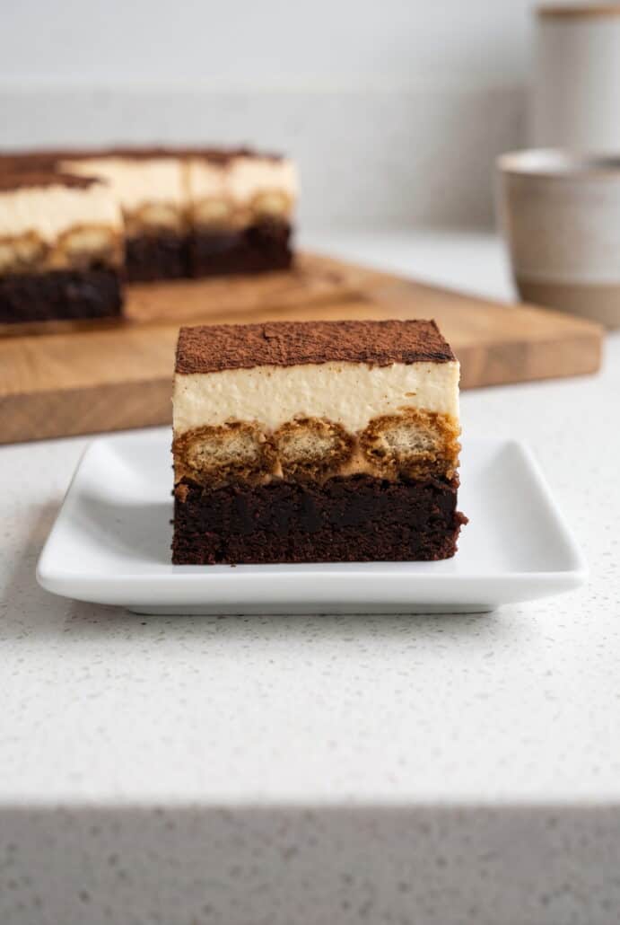 Tiramisu brownie square with fudgy chocolate base, espresso-soaked ladyfingers, mascarpone cream, and cocoa topping.