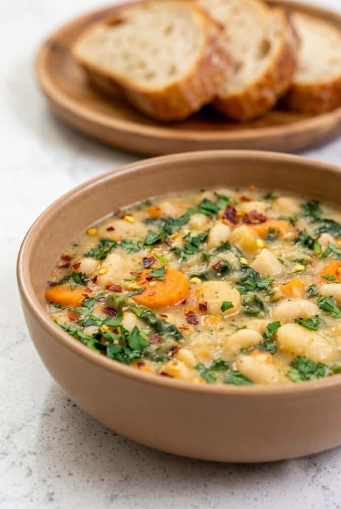 Bowl of creamy Tuscan white bean soup with cannellini beans, carrots, kale, and herbs.