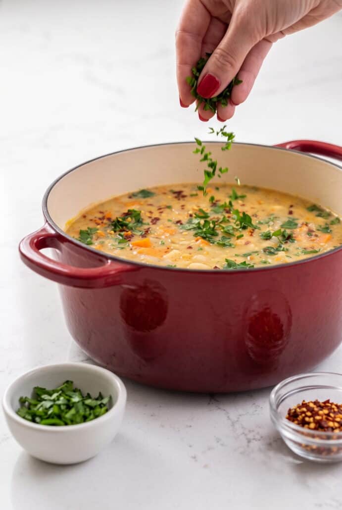 Creamy Tuscan white bean soup served in a red Dutch oven with kale and herbs, ready for a cozy family dinner.