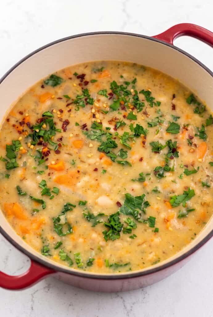 Close-up of creamy Tuscan white bean soup with carrots, kale, and herbs in a Dutch oven.