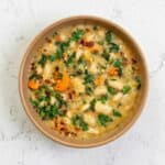 Bowl of creamy Tuscan white bean soup with carrots, kale, and herbs, showcasing this hearty one-pot vegetarian soup recipe perfect for a cozy meal.