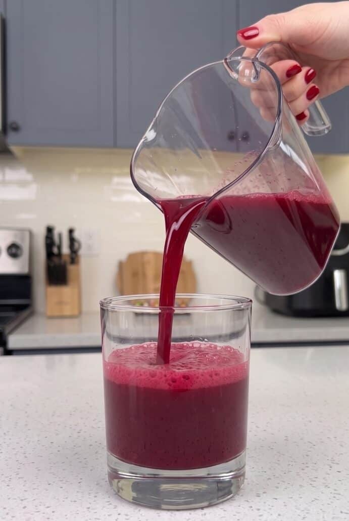 Watermelon cherry berry beet juice being poured from a pitcher into a glass.