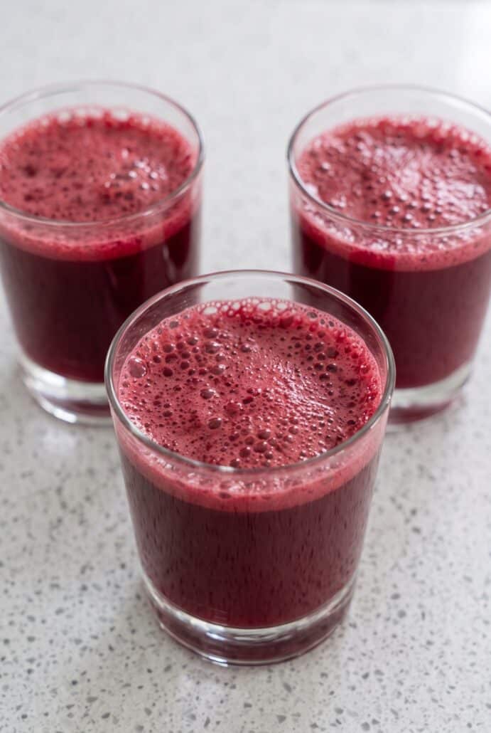 Three glasses of freshly made watermelon cherry berry beet juice with a frothy top.