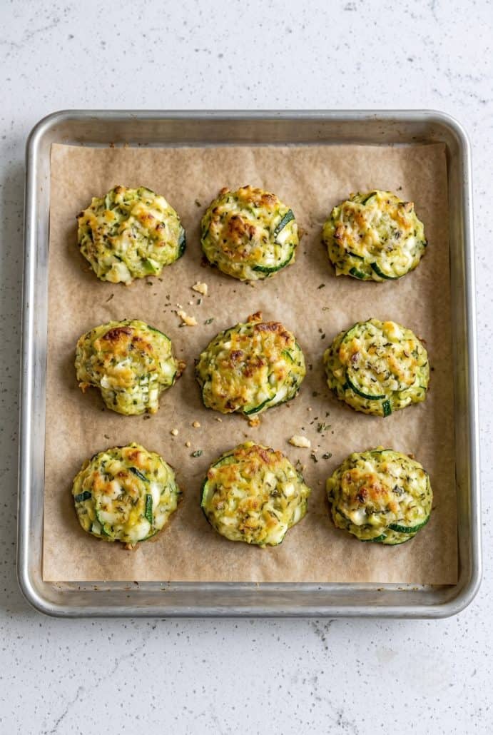 Baked zucchini garlic bites cooling on a parchment-lined baking sheet.