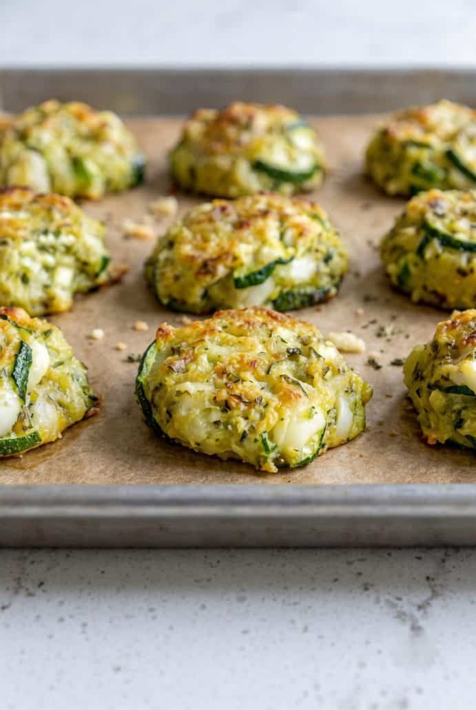 Golden zucchini garlic bites baked with herbs and Parmesan on a lined baking sheet.