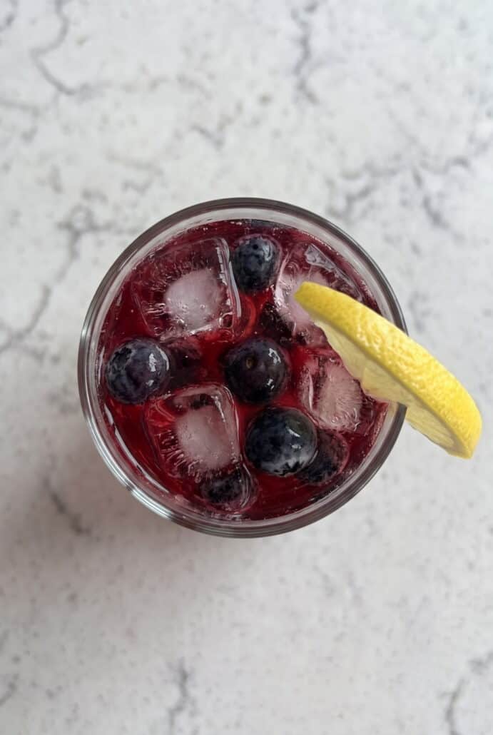 Top view of blueberry lemonade with fresh blueberries, ice, and a lemon wedge.