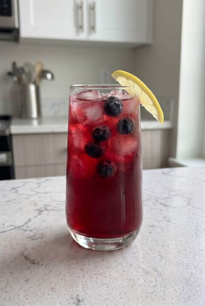 Glass of homemade blueberry lemonade with fresh blueberries, ice, and a lemon slice garnish.