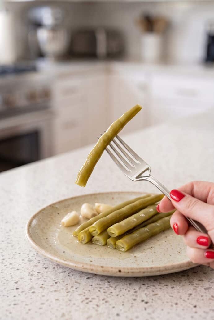 Dill pickled green bean being lifted from the jar, showing its crisp texture and ready-to-eat serving.