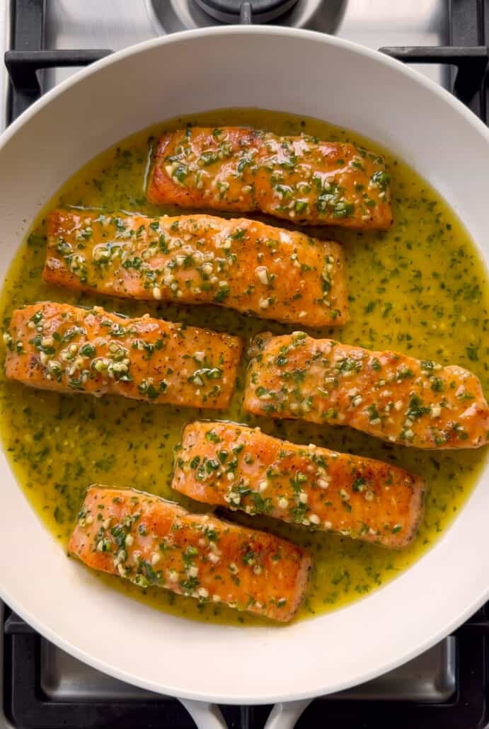 Garlic butter salmon fillets simmering in a rich herb sauce.