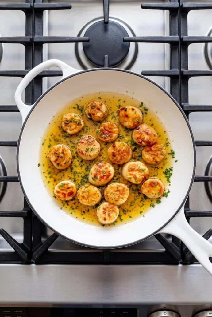 Garlic butter scallops searing in a skillet with lemon garlic butter sauce and fresh parsley.