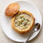 Homemade bread bowl filled with creamy soup, served with the bread top on the side.