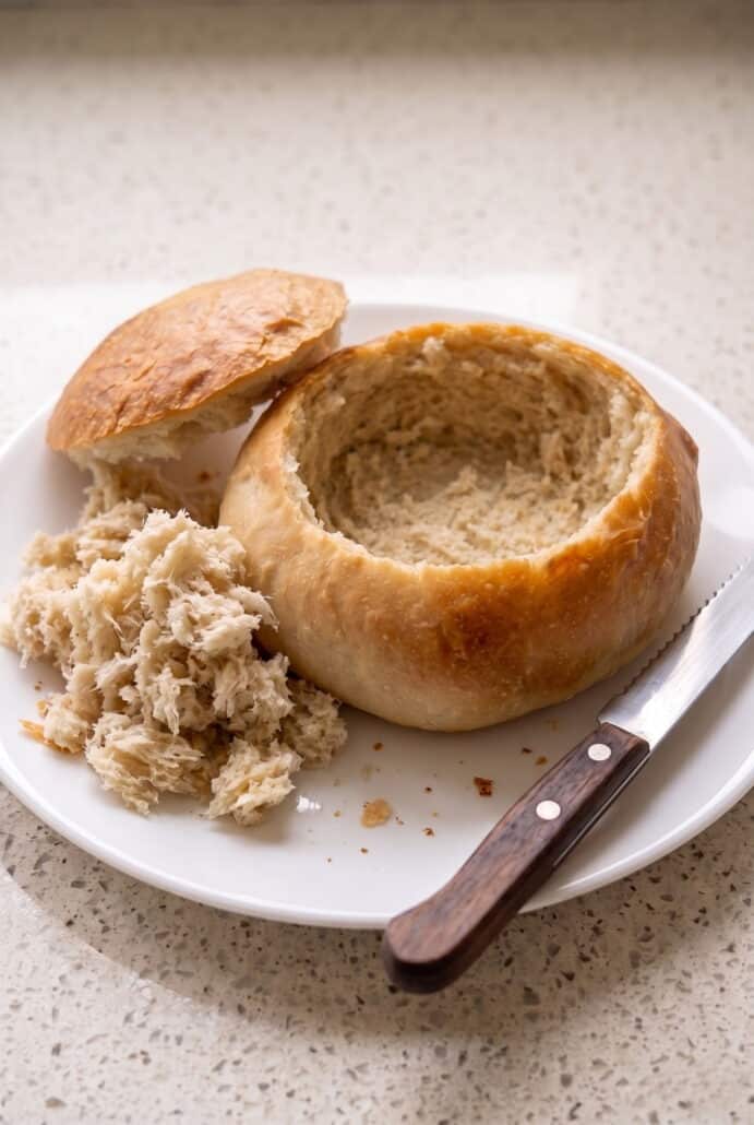 Hollowed homemade bread bowl ready to fill with soup, with the bread top and scooped-out pieces on the side.