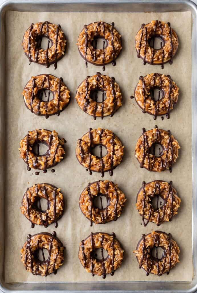 Homemade Samoas cookies topped with caramel, toasted coconut, and chocolate drizzle on a baking sheet.