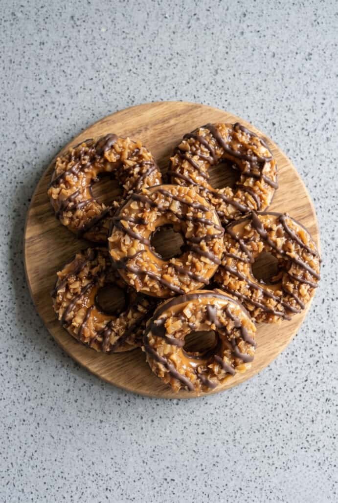 Homemade Samoas cookies with caramel, toasted coconut, and chocolate drizzle arranged on a wooden serving board.