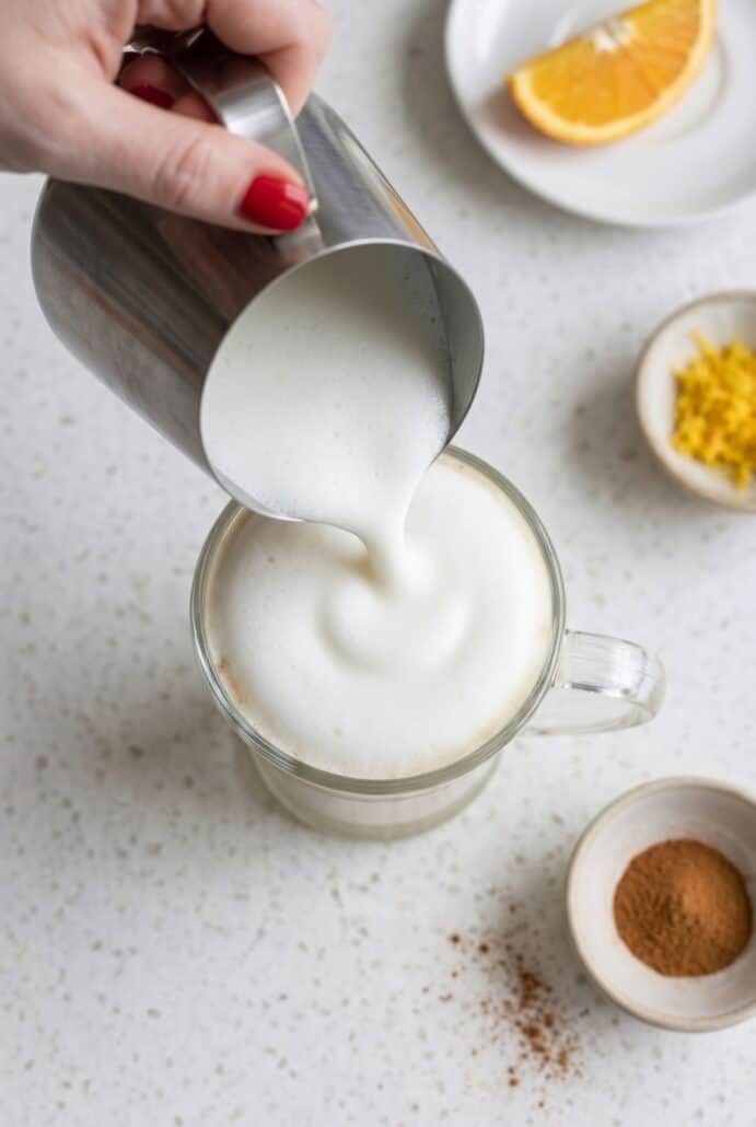 Milk being poured into a cup to prepare white chocolate orange hot cocoa.