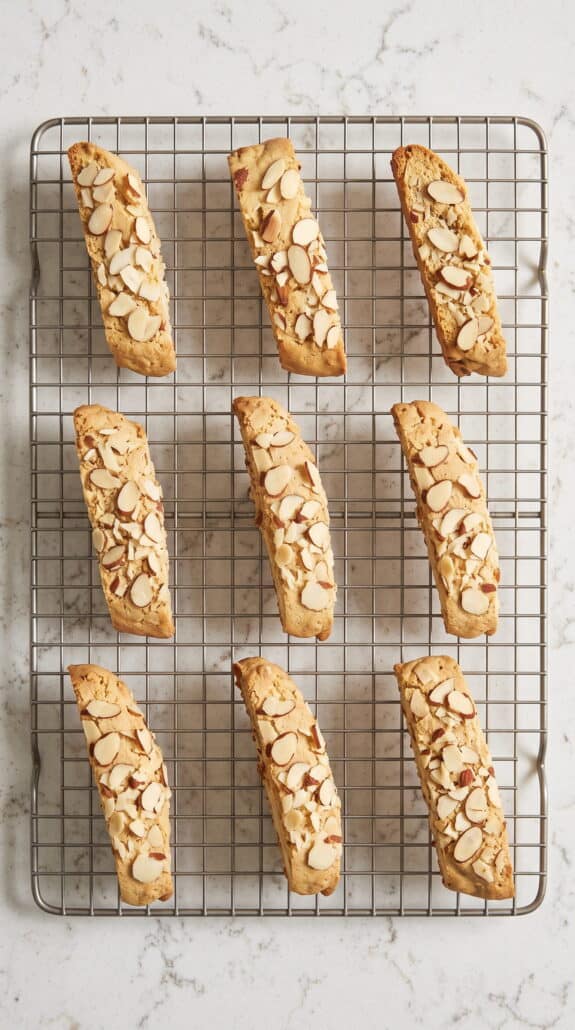 Freshly baked almond biscotti topped with sliced almonds cooling on a wire rack.