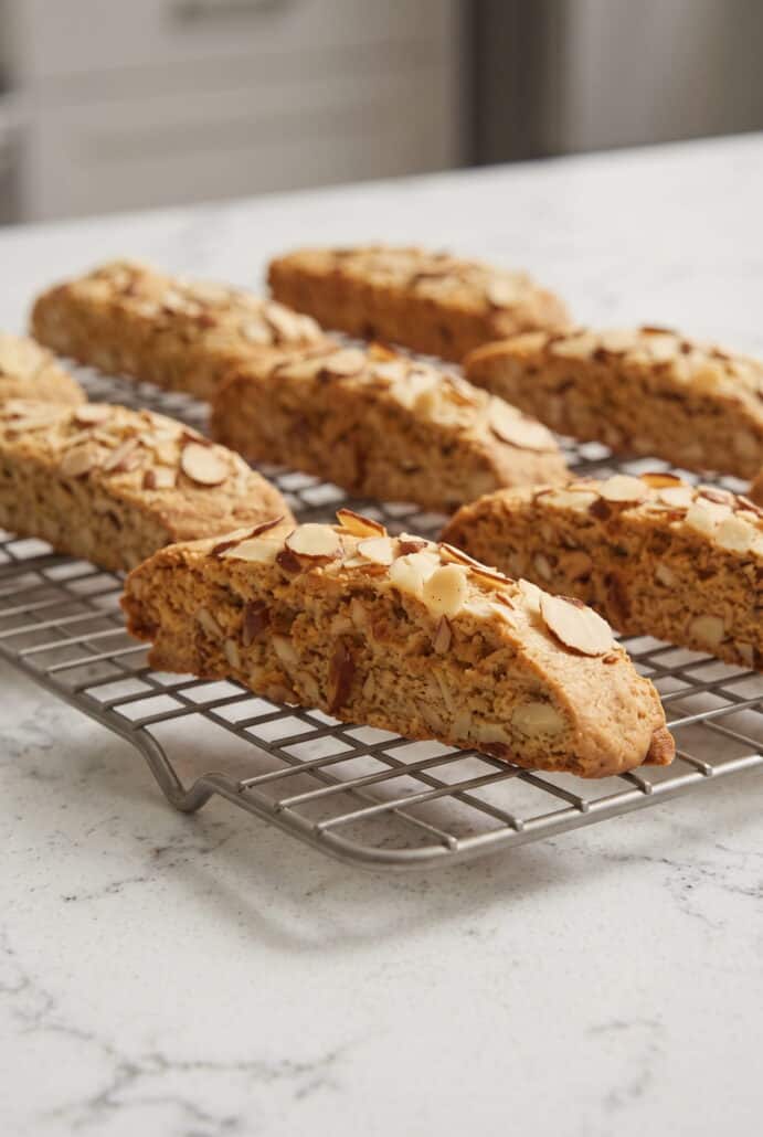 Golden almond biscotti with sliced almonds cooling on a wire rack after baking.