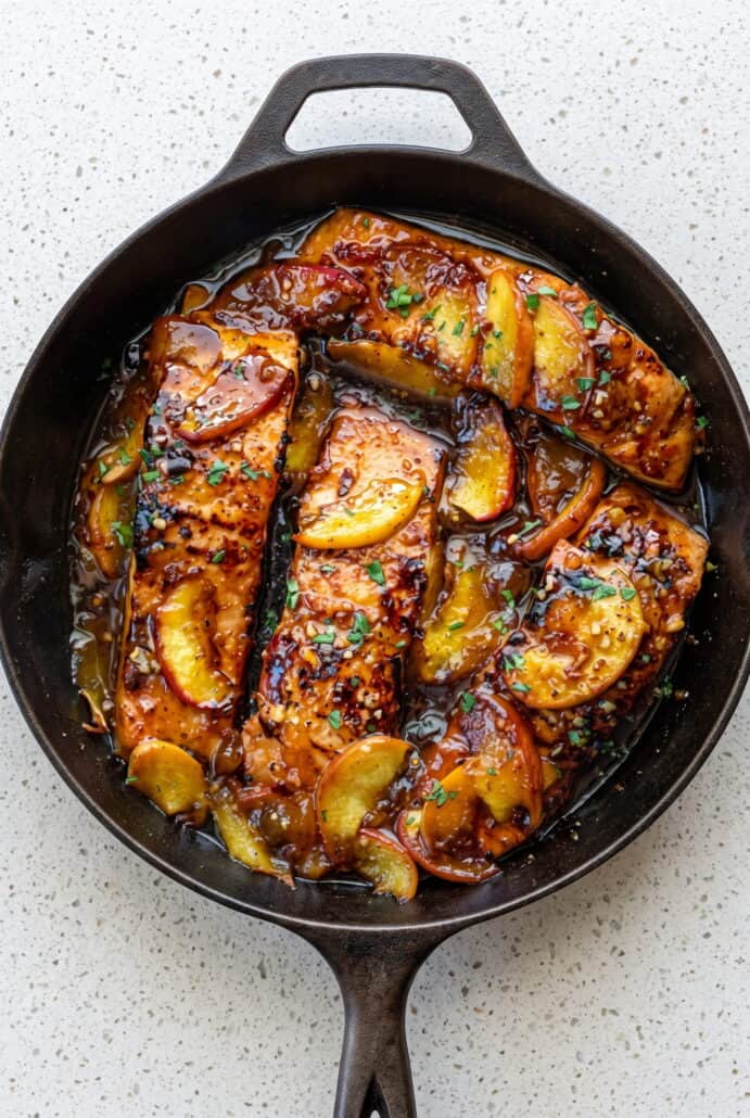 Bourbon peach roasted salmon in a skillet with caramelized peach slices and glossy glaze.