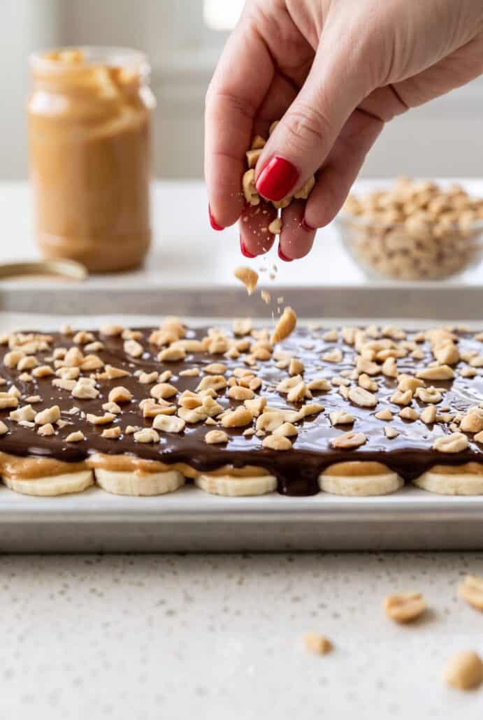 Sprinkling chopped peanuts over chocolate banana bark before freezing for an easy dessert.