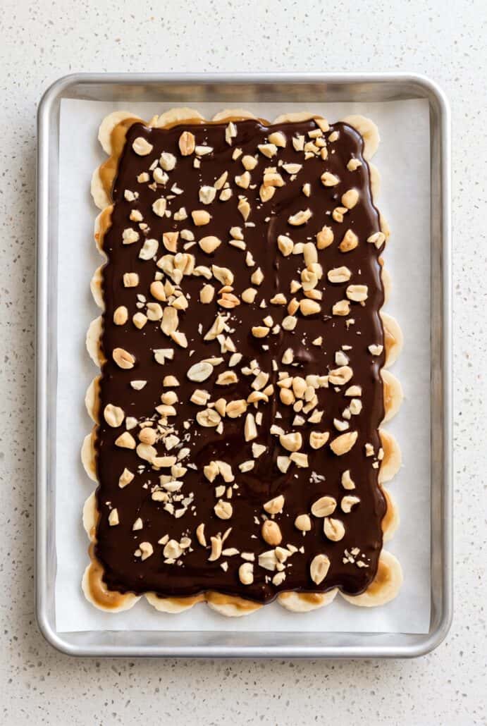 Chocolate banana bark covered with dark chocolate and chopped peanuts on parchment paper, ready to freeze and break into pieces.