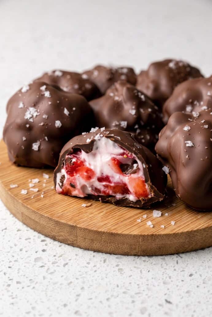 Chocolate-covered strawberry yogurt bites with one cut open to show the creamy strawberry filling.