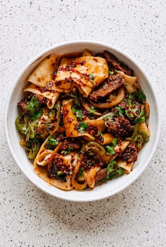 Restaurant Style Cumin Lamb Noodles at Home Cumin lamb noodles with tender lamb, wide noodles, onions, greens, and spicy chili seasoning.