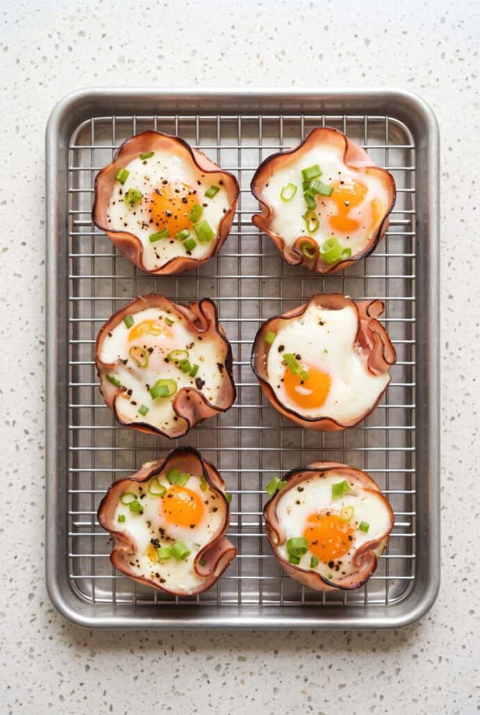 Baked ham and cheese egg cups topped with green onions on a cooling rack.
