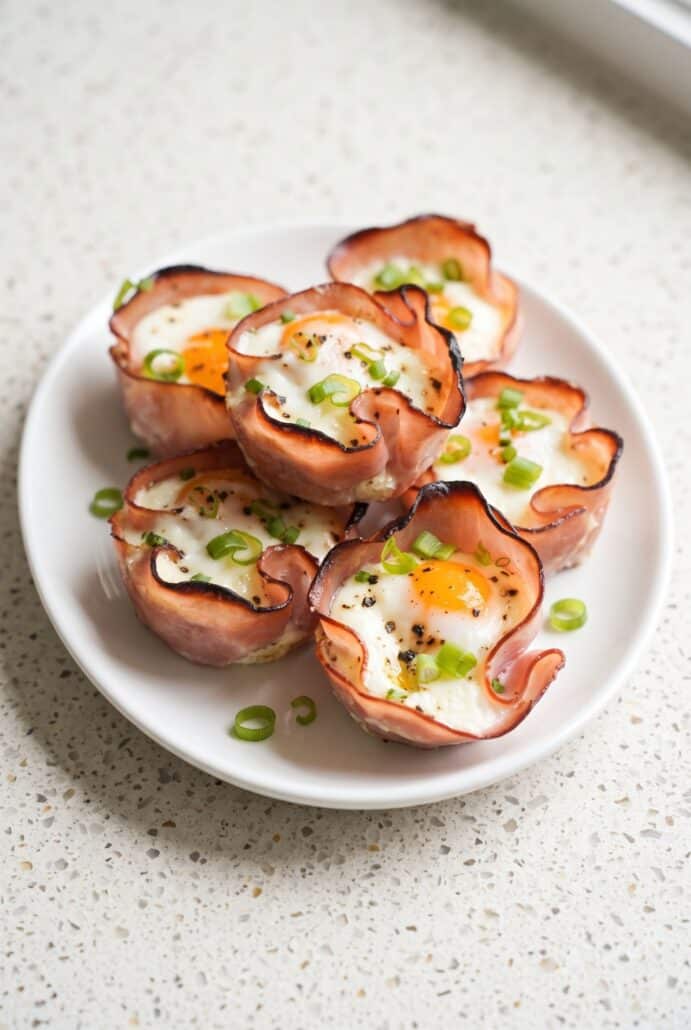 Ham and cheese egg cups stacked on a plate and topped with green onions for breakfast.