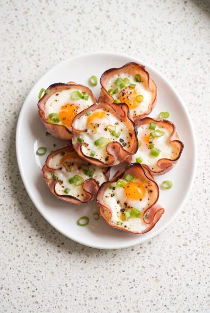 Ham and cheese egg cups served on a plate with green onions for a savory breakfast.