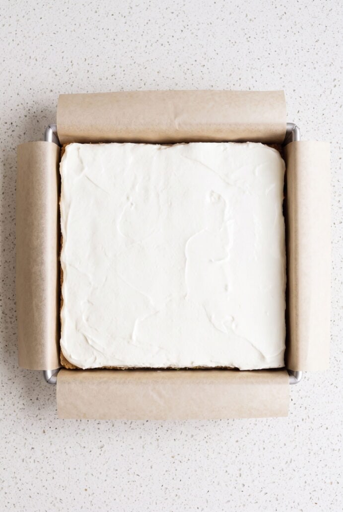 Key lime pie bars topped with smooth whipped cream in a parchment-lined baking pan.