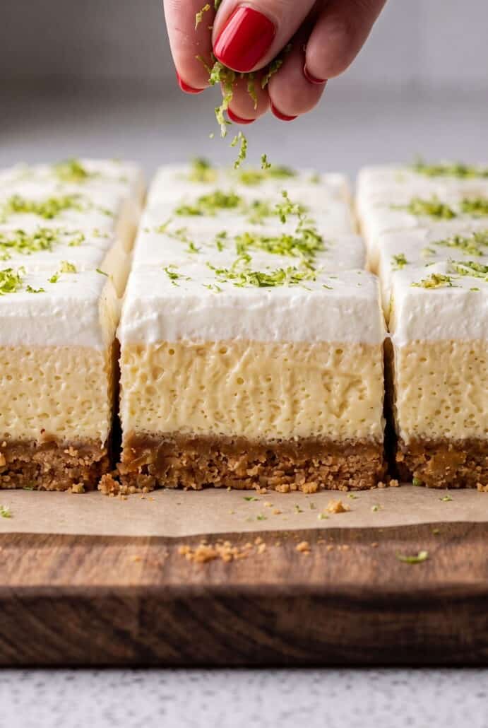 Layered key lime pie bars with creamy lime filling, whipped topping, and fresh lime zest over a cookie crust.