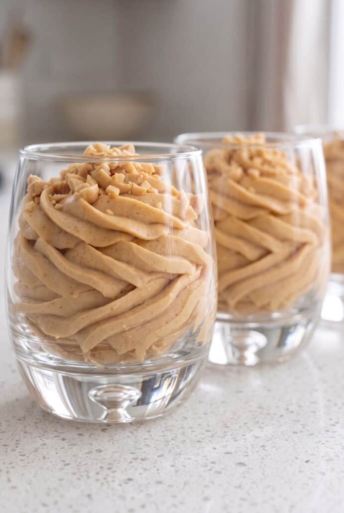 Close-up of fluffy peanut butter mousse swirled in glasses and topped with chopped peanuts.
