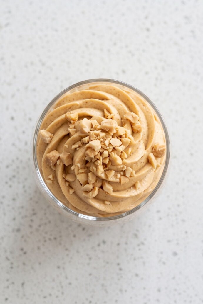 Top view of creamy peanut butter mousse topped with chopped peanuts in a glass.