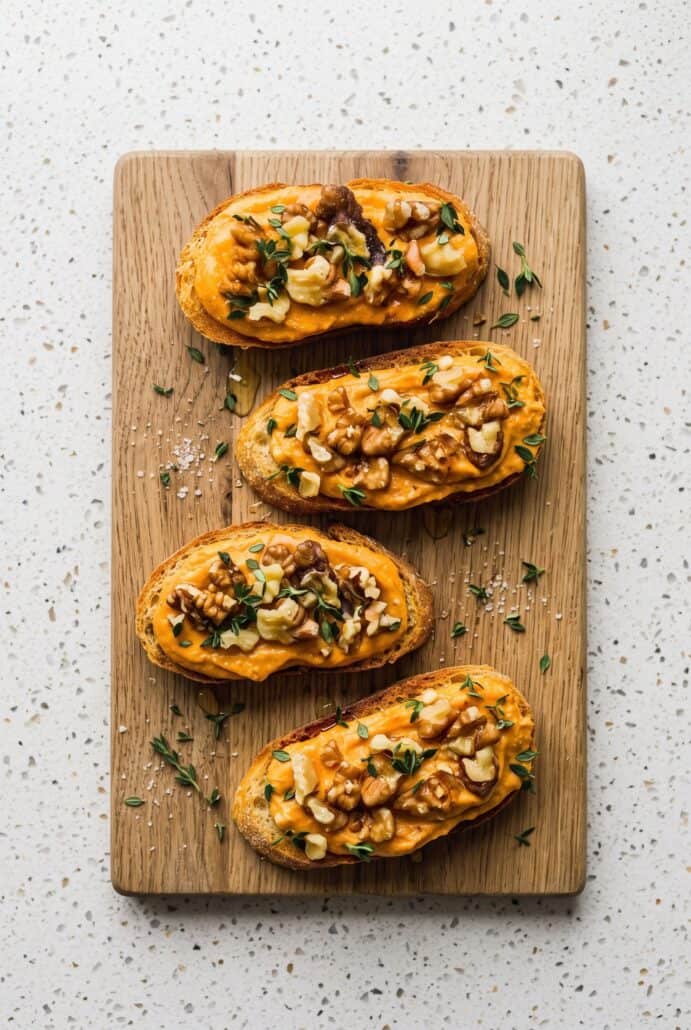 Pumpkin whipped feta crostini topped with walnuts, fresh thyme, and honey for an easy fall appetizer.