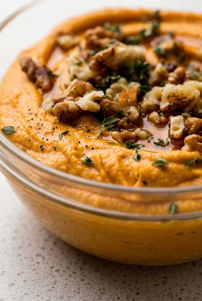 Close-up of creamy pumpkin whipped feta topped with chopped walnuts, thyme, and honey for a festive fall appetizer.