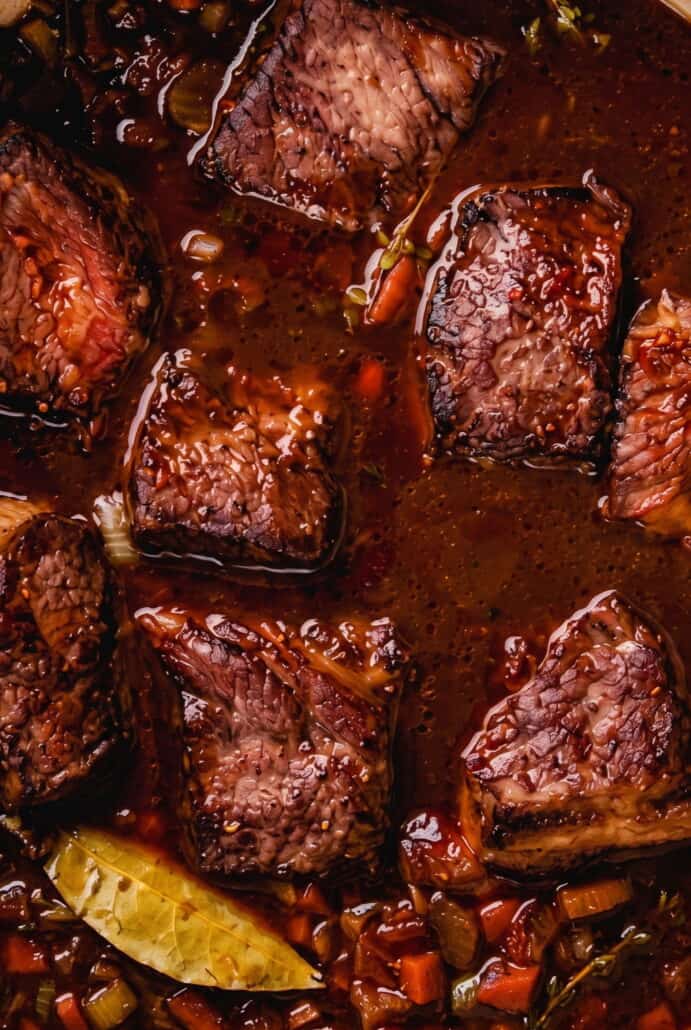 Tender red wine braised short ribs in rich sauce after slow cooking in a Dutch oven.