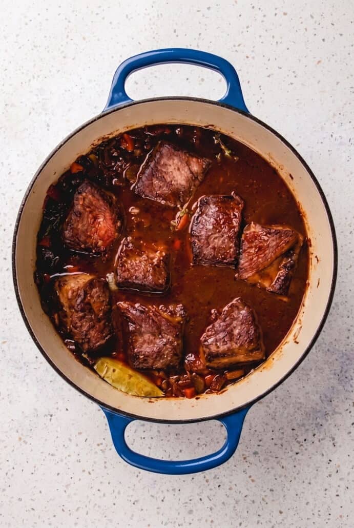 Red wine braised short ribs simmering in a Dutch oven with rich savory sauce.