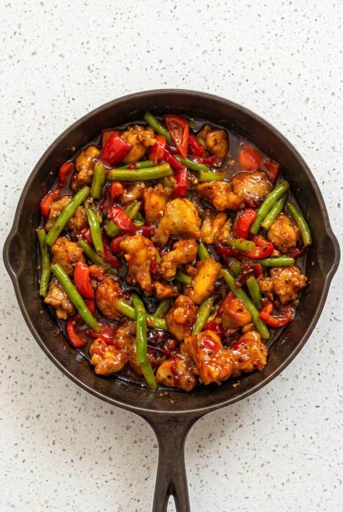 Sweet chili chicken and green bean stir fry with colorful bell peppers in a skillet.