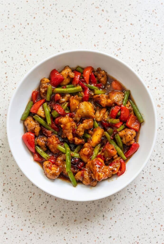 Sweet chili chicken and green bean stir fry with red bell peppers served in a white bowl.