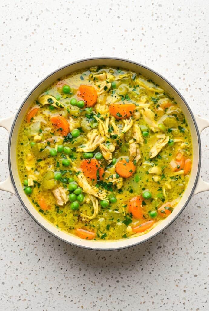 Bowl of turmeric chicken soup with shredded chicken, carrots, peas, and fresh herbs in a golden broth.