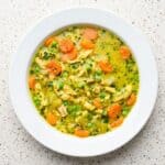 Turmeric chicken soup with tender chicken, carrots, peas, and herbs in a golden broth.