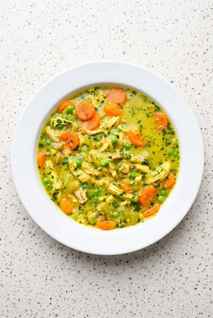 Turmeric chicken soup with tender chicken, carrots, peas, and herbs in a golden broth.