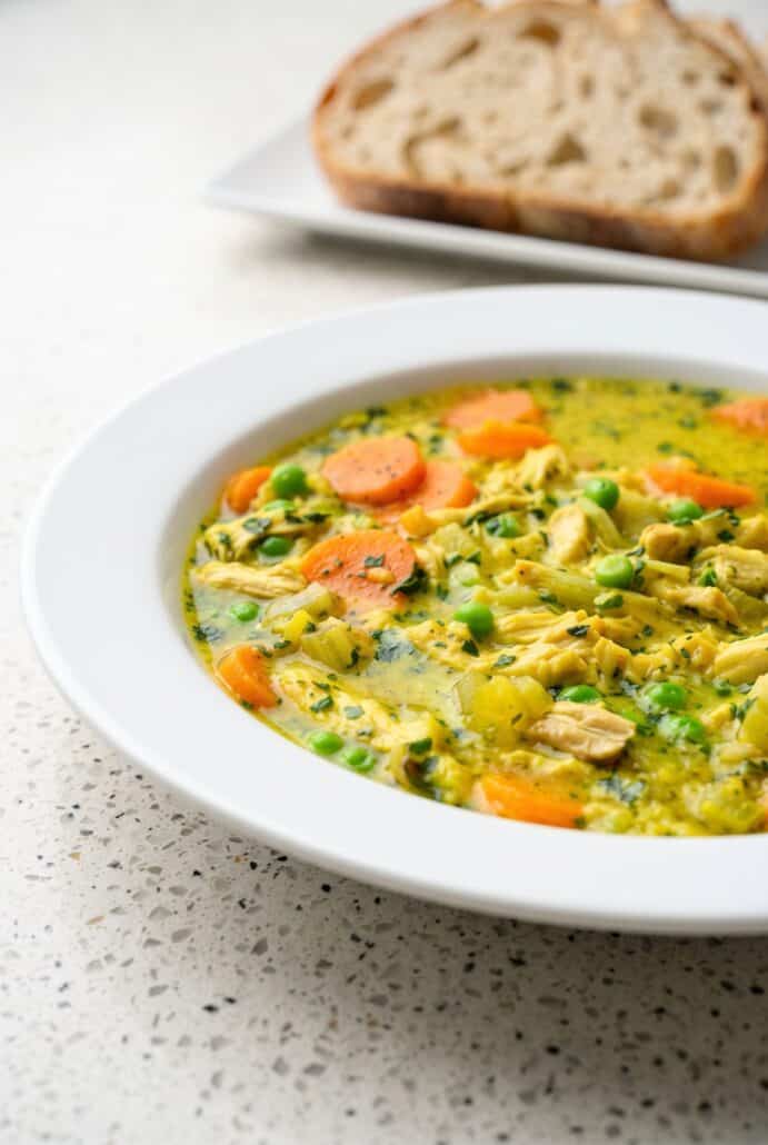 Turmeric chicken soup with shredded chicken, carrots, peas, and herbs in a creamy golden broth.