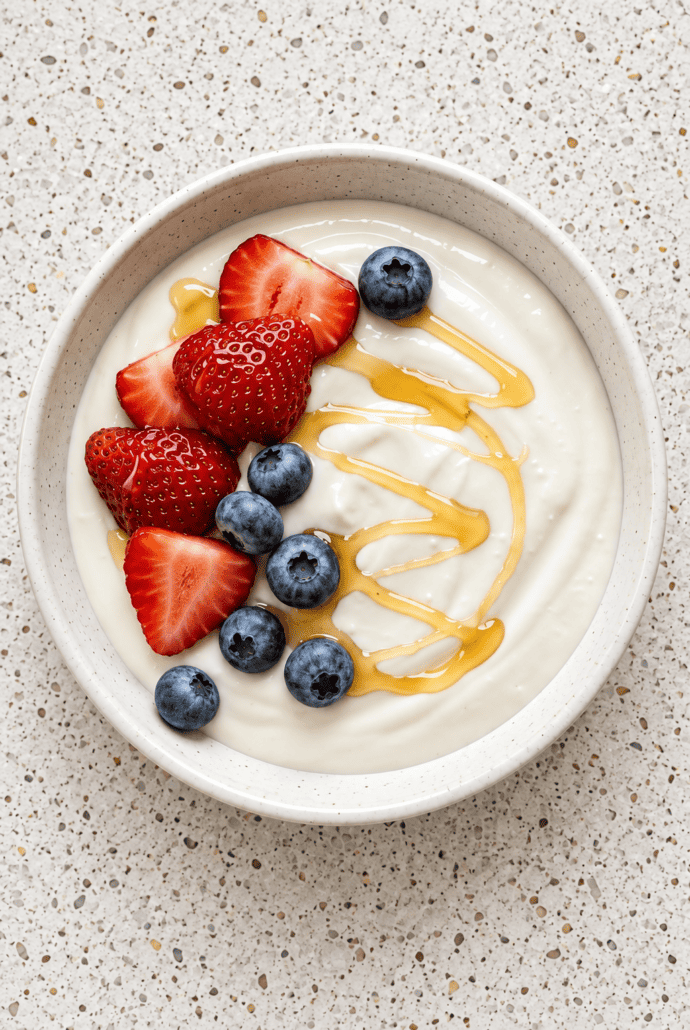 Instant Pot yogurt topped with fresh strawberries, blueberries, and a drizzle of honey for serving.